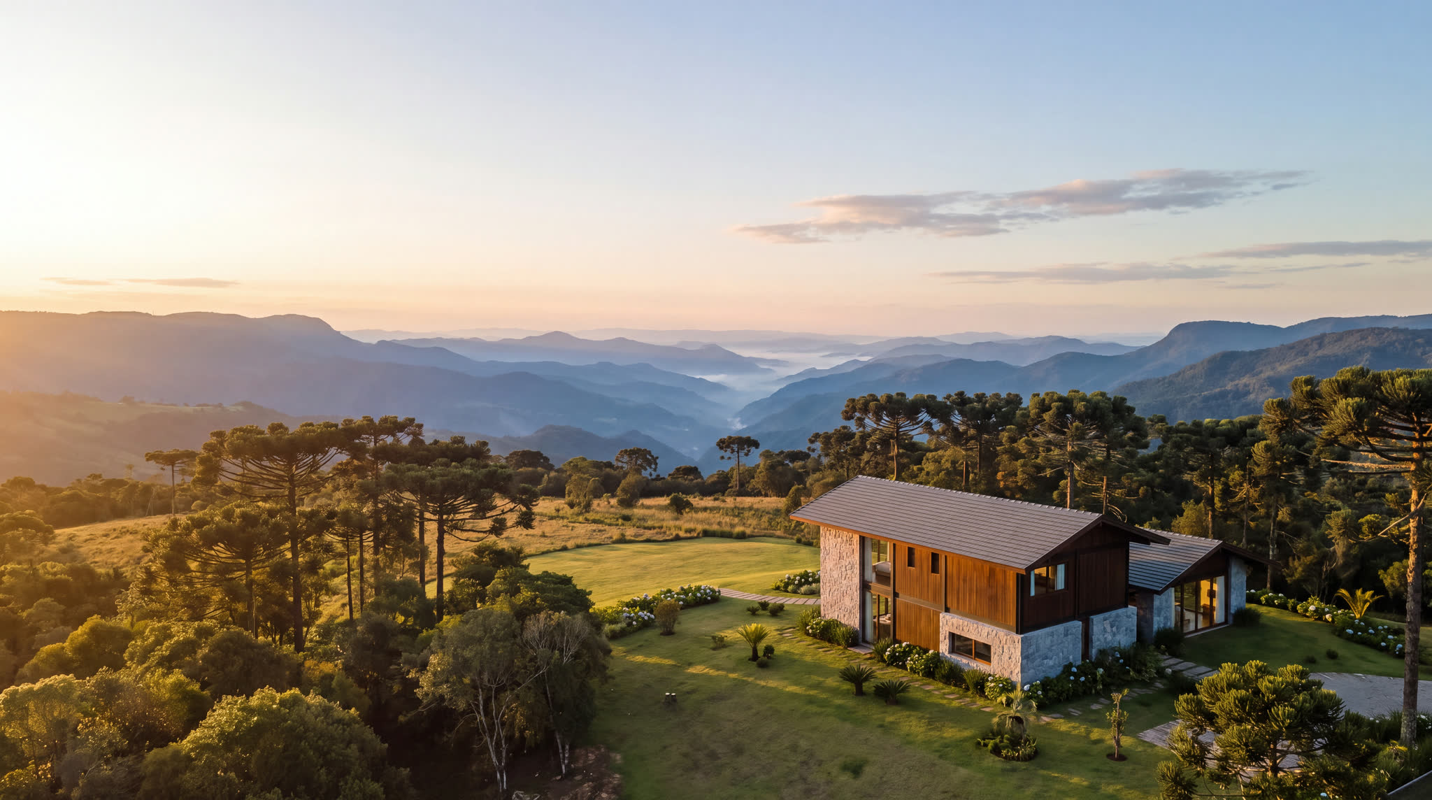 Casa contemporânea em um platô da Serra da Mantiqueira, com araucárias e um vale de montanhas em camadas ao pôr do sol